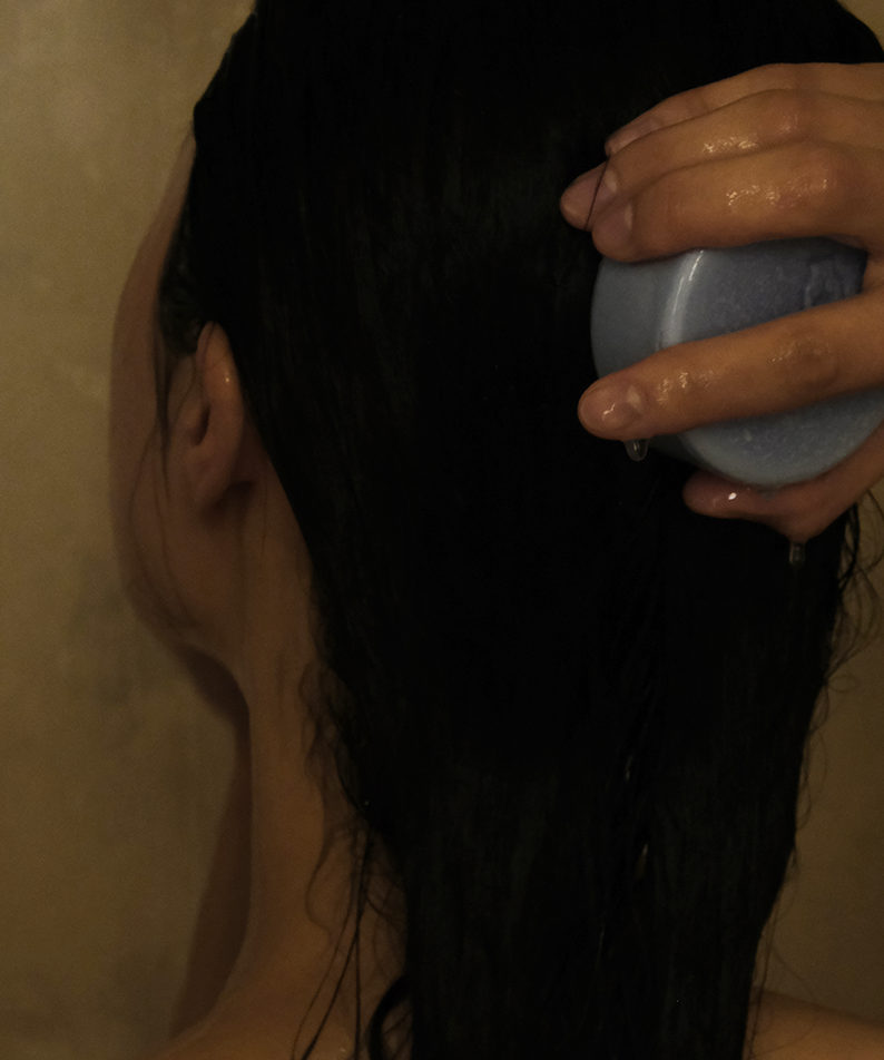 DONGGUBAT Field Correct Rinse Bar : main tenant la barre avec cheveux, contexte douche/salle de bain, marque DONGGUBAT.