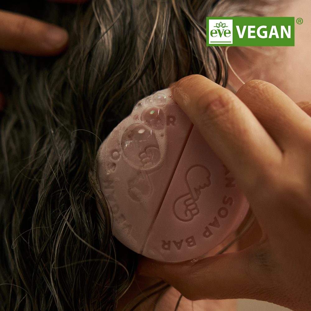 DONGGUBAT Vegan Shampoo Bar Dongbaek de la marque, barrette de shampooing tenant dans les mains, cheveux en arrière-plan.