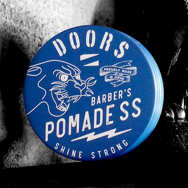 DOORS Original Pomade SS 120g, pot bleu DOORS Barbers, contexte barber shop, photo gros plan sur l’étiquette.