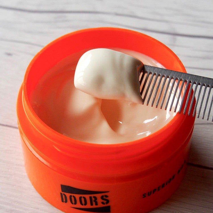 DOORS Superior Wax Monster Hold 80g, cire coiffante DOORS dans un pot orange sur table en bois, gros plan.