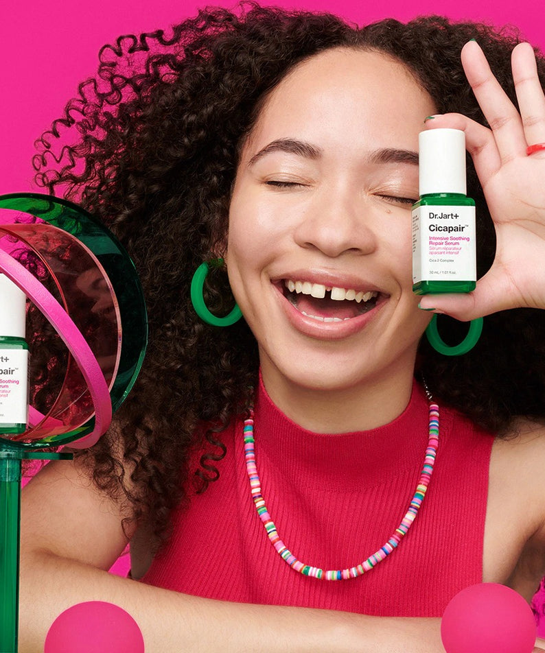 Sérum apaisant DR.JART+ CicapairI ntensive Soothing Repair Serum 30ml tenu par une femme souriante, fond rose vif.