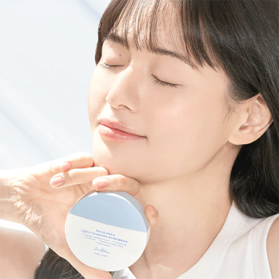 Décris l'image en français : DR.ALTHEA Aqua Glowing Sunscreen 45ml, crème solaire brillante, visage en lumière du soleil.
