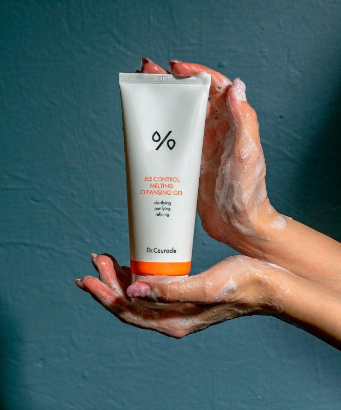 DR.CEURACLE 5 Alpha Control Melting Cleansing Gel 150ml, tube sur mains avec mousse, fond bleu, contexte beauté.