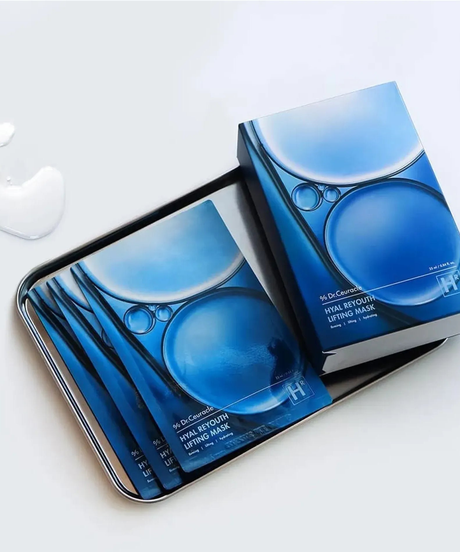 Décris l'image en français : DR.CEURACLE Hyal Reyouth Lifting Mask (10EA), marque sur coffret bleu, masques sur plateau.