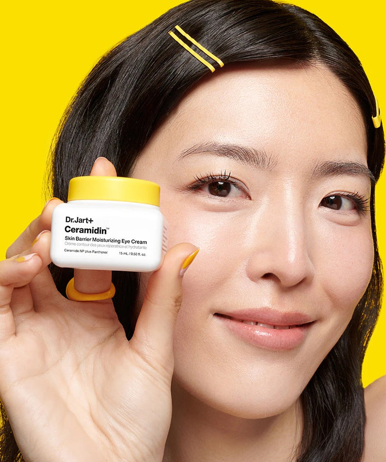 Décris l'image en français : DR.JART+ Ceramidin Skin Barrier Moisturizing Eye Cream 15ml, femme montrant le pot sur fond jaune.