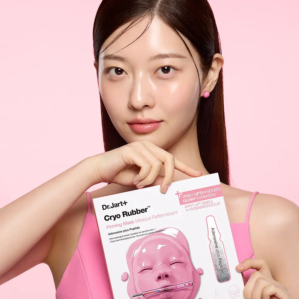 Décris l'image en français : DR.JART+ Cryo Rubber Masks 4 Types, masque et pack, visage d'une femme sur fond rose.