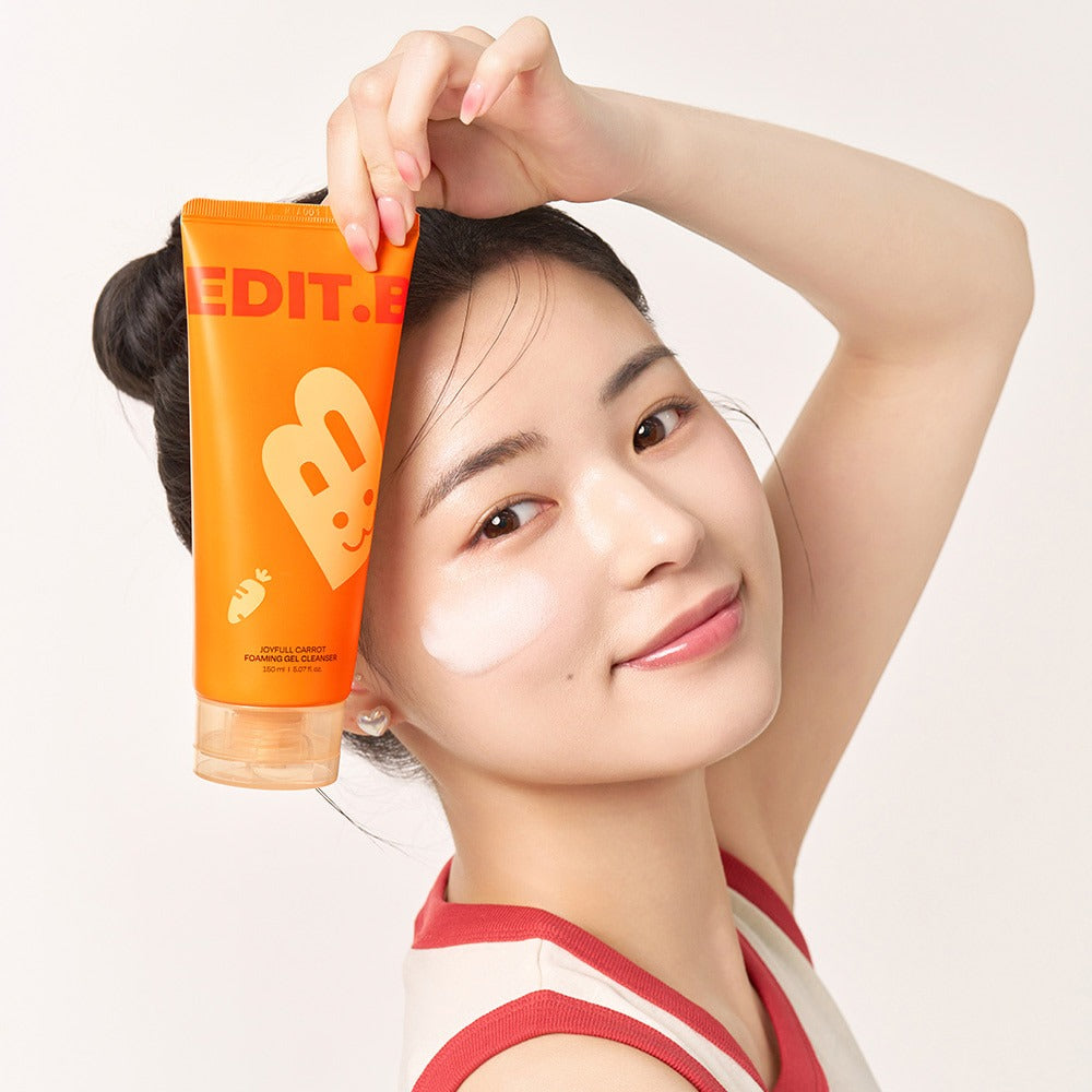 EDIT.B Joyful Carrot Foaming Gel Cleanser 150ml de la marque EDIT.B sur peau, tube orange, visage féminin souriant, fond clair