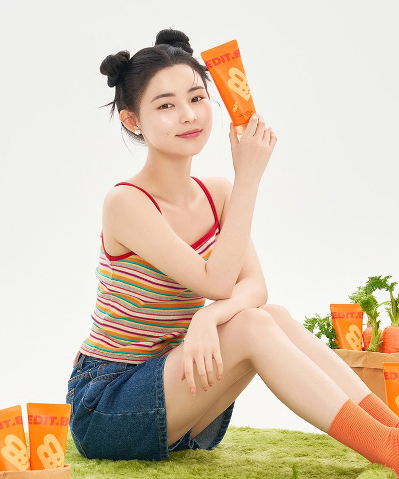 EDIT.B Joyful Carrot Foaming Gel Cleanser 150ml de la marque EDIT.B : femme tient le flacon, fond herbe, carottes visibles.