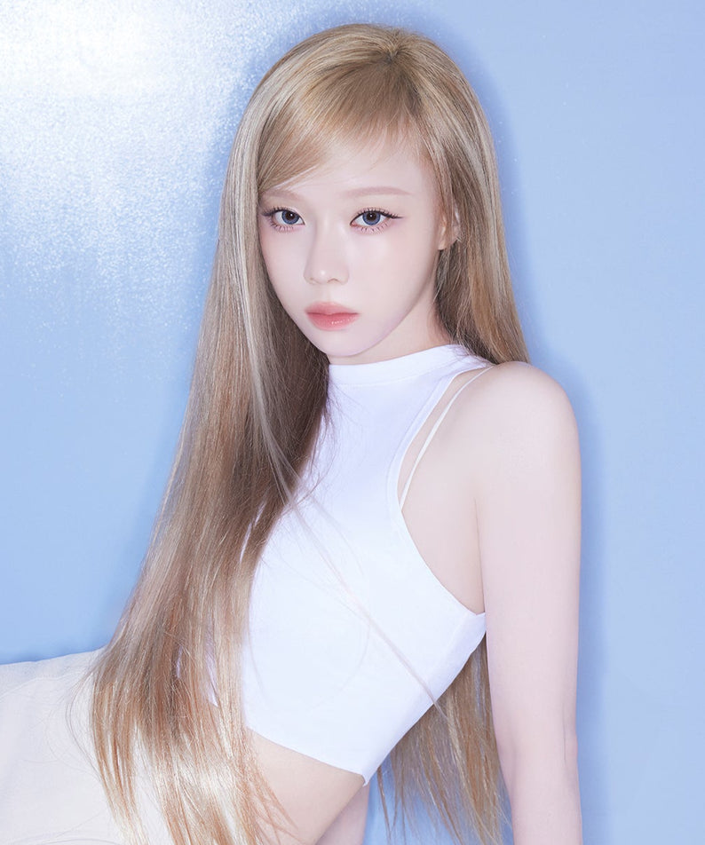 Jeune femme posant devant un mur bleu, portant un débardeur blanc et ayant de longs cheveux blonds.