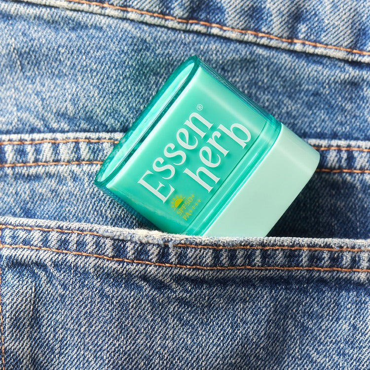 ESSENHERB  Multi Defense Cloud Fit Airy Sun Stick 10g, stick solaire vert sur jean, marque visible, contexte plein cadrage.