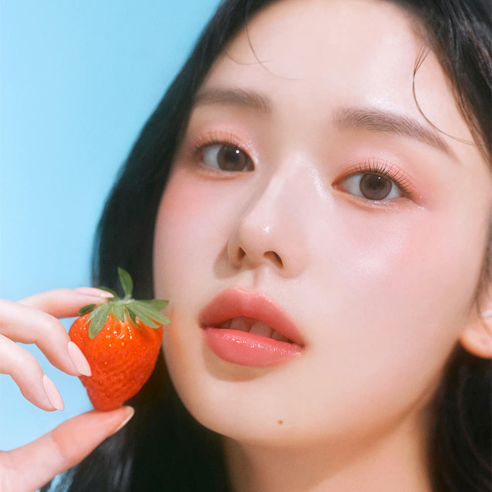 ETUDE Dear Darling Oil Tint : jeune femme maquillée tenant une fraise, fond bleu, huile teintée de la marque ETUDE.