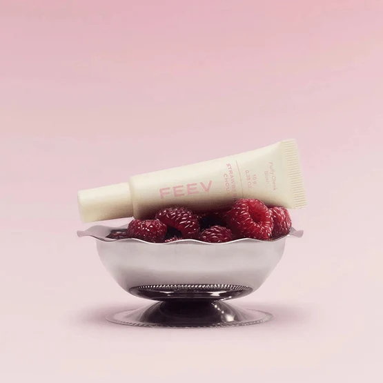 Décris l'image en français : FEEV Fluffy Cheek Blush 10g de la marque FEEV, tube beige sur framboises roses.