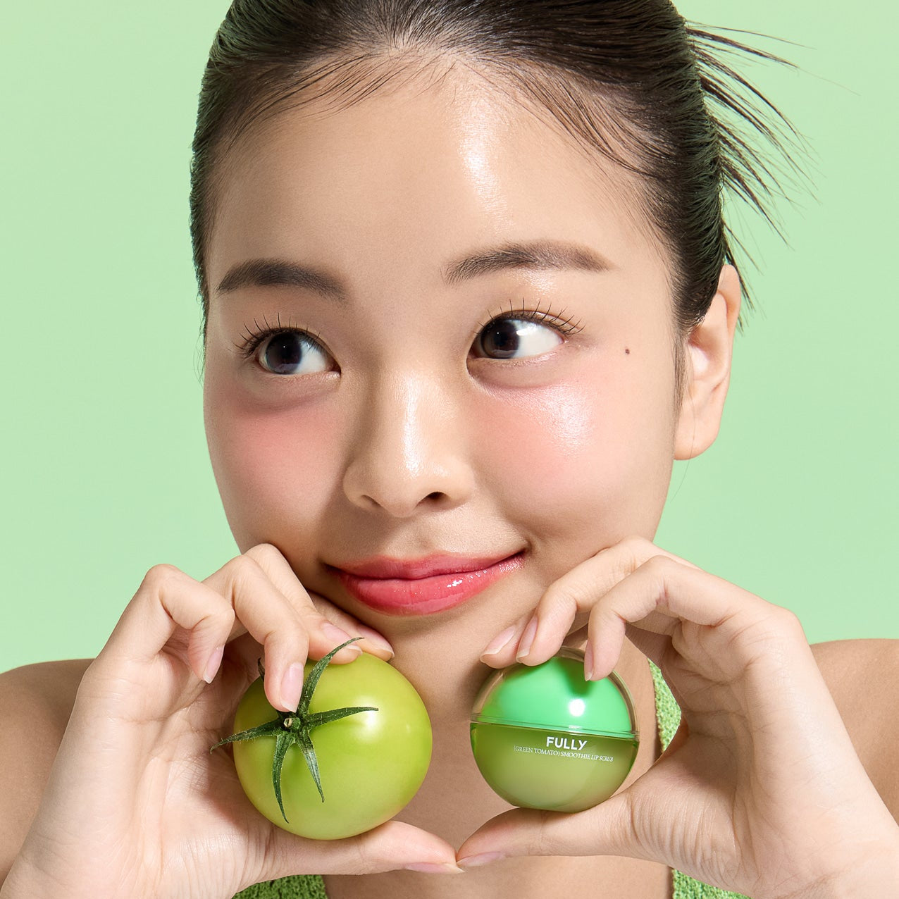 Décris l'image en français : FULLY Green Tomato Smoothie Lip Scrub 12g de la marque FULLY, pots verts sur fond vert.