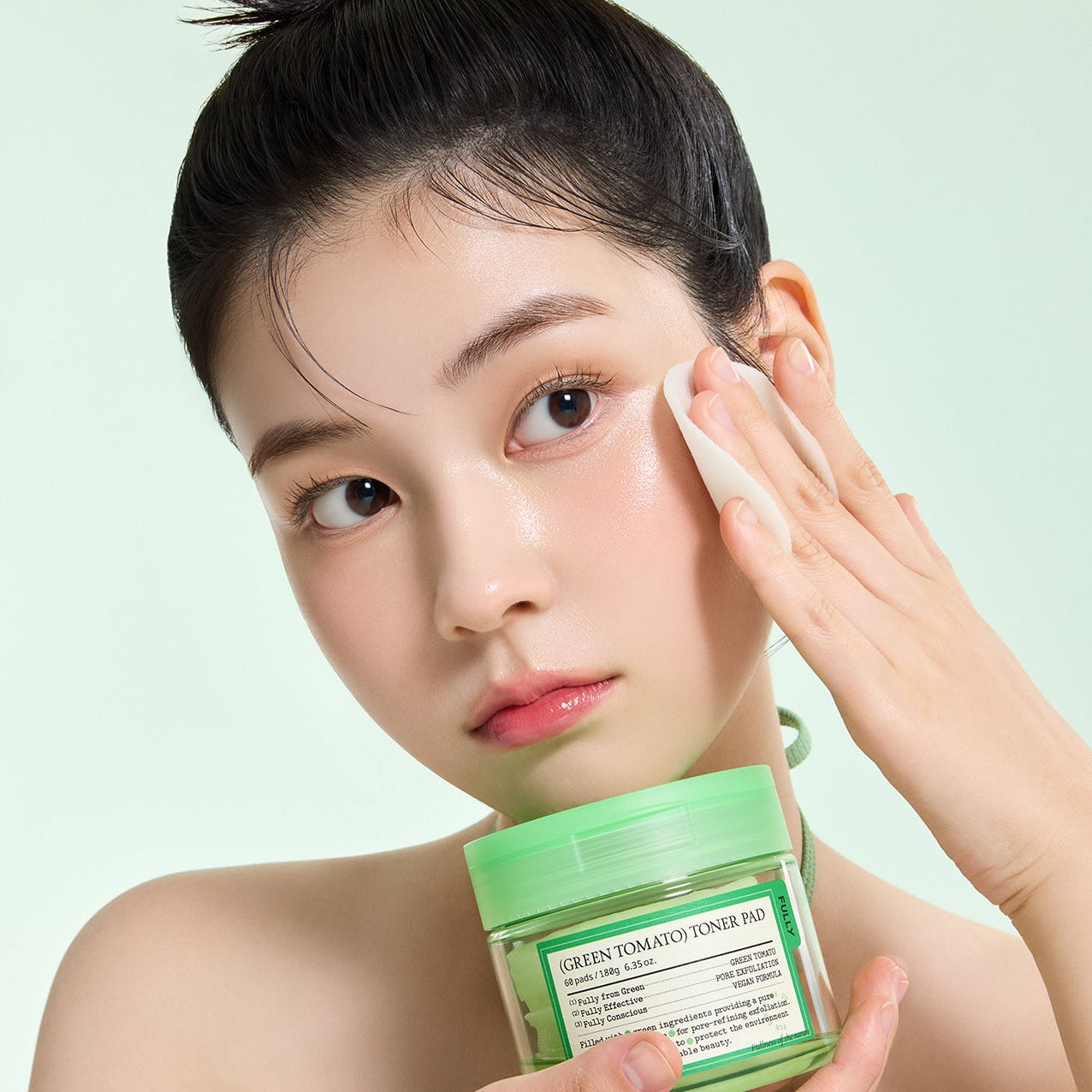 FULLY Green Tomato Toner Pads 60 Sheets, marque FULLY : femme applique les pads sur le visage, pot vert en arrière-plan