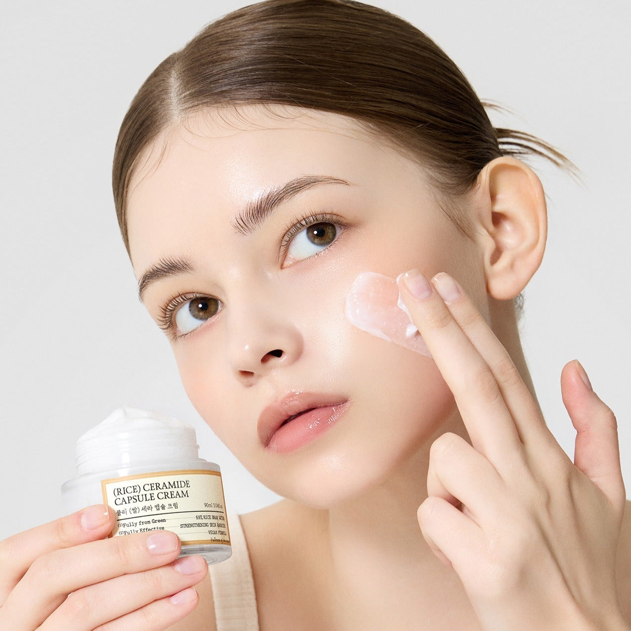 FULLY  Rice Sera Capsule Cream 90ml, crème skincare FULLY appliquée sur le visage, femme au geste de soin, fond clair.