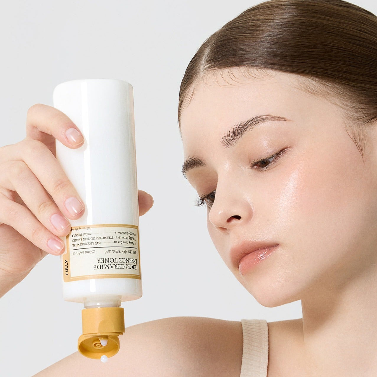 FULLY Rice Serum Essence Toner 250ml de la marque FULLY, femme applique le soin sur fond clair, packaging en main
