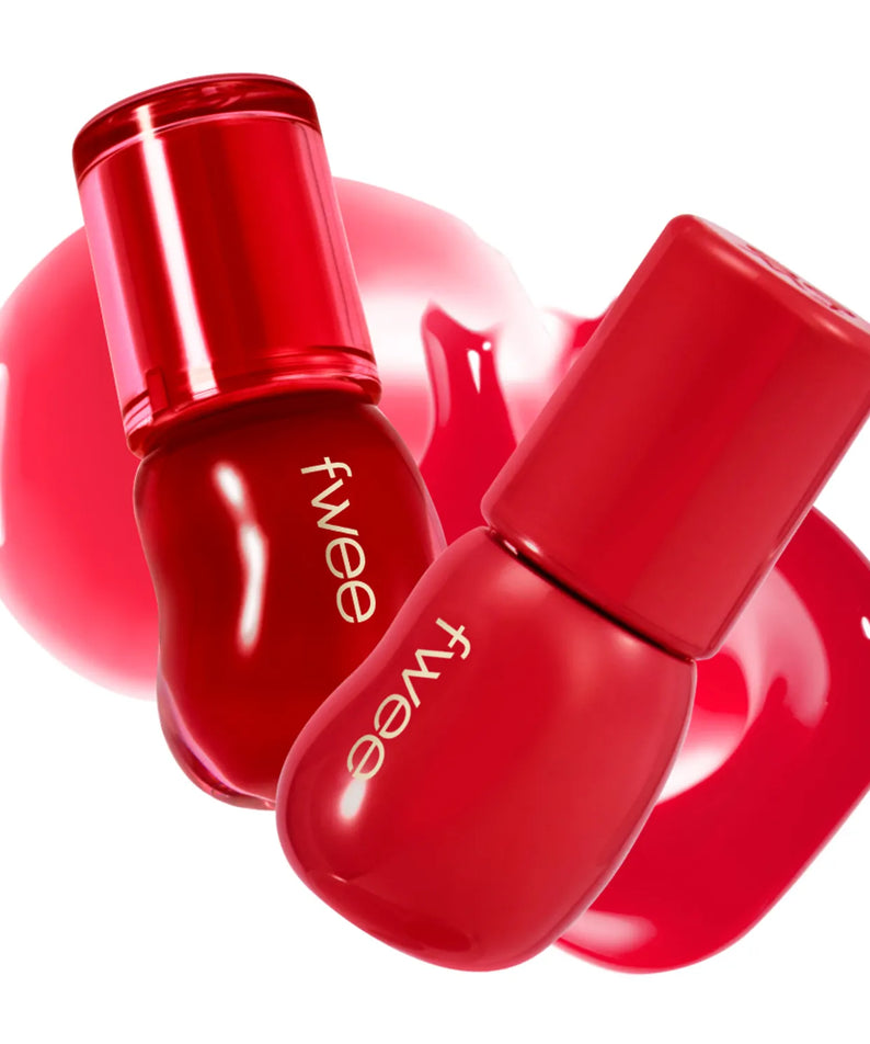 Deux flacons de FWEE 3D Voluming Gloss rouges avec effet volumisant et brillant, posés sur des éclaboussures de gloss rose vif.