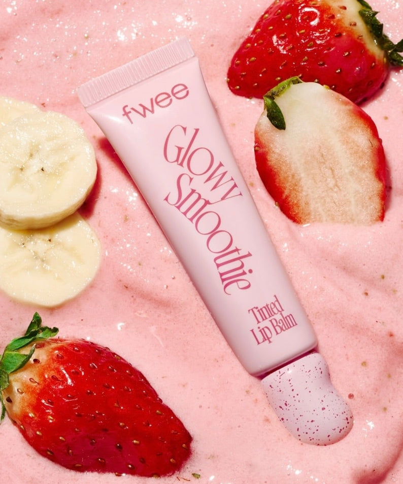FWEE Glow Smoothie Tinted Lip Balm de la marque FWEE, sur fond rose avec fraises et tranches de banane.