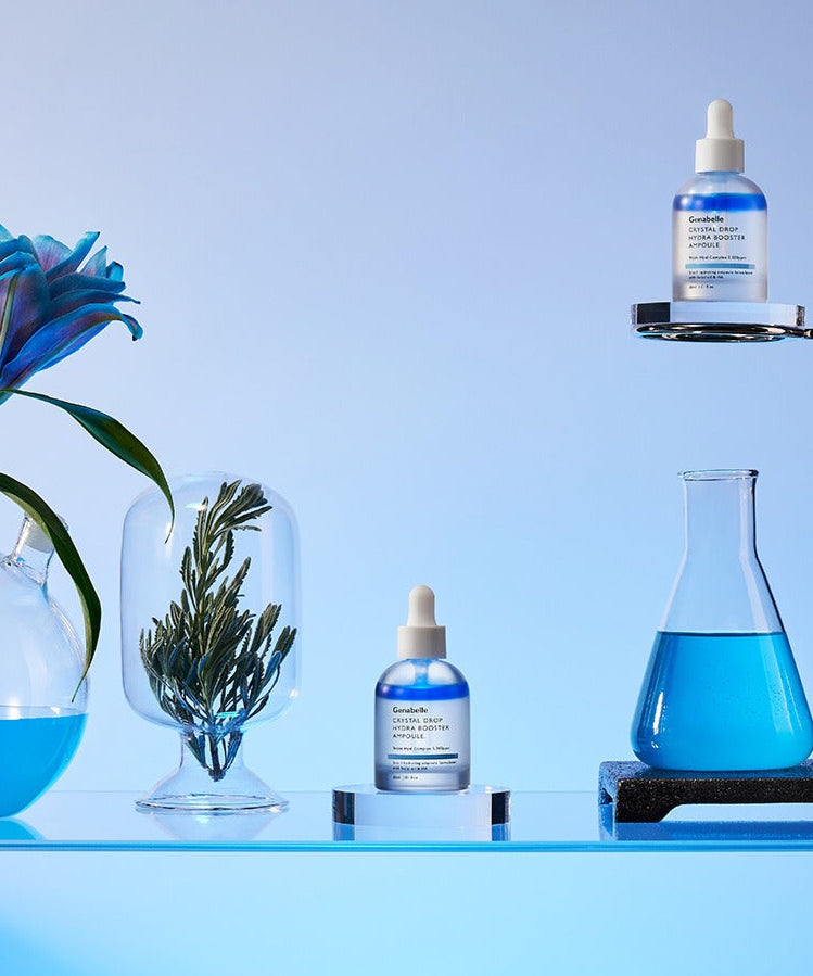 GENABELLE Crystal Drop Hydra Booster Ampoule 30ml mise en scène avec des éléments scientifiques et fleurs sur fond bleu.