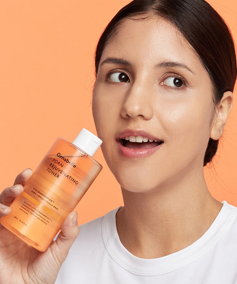 Femme souriante tenant un flacon de GENABELLE PDRN Rejuvenating Toner 300ml sur fond orange, produit de soin revitalisant.