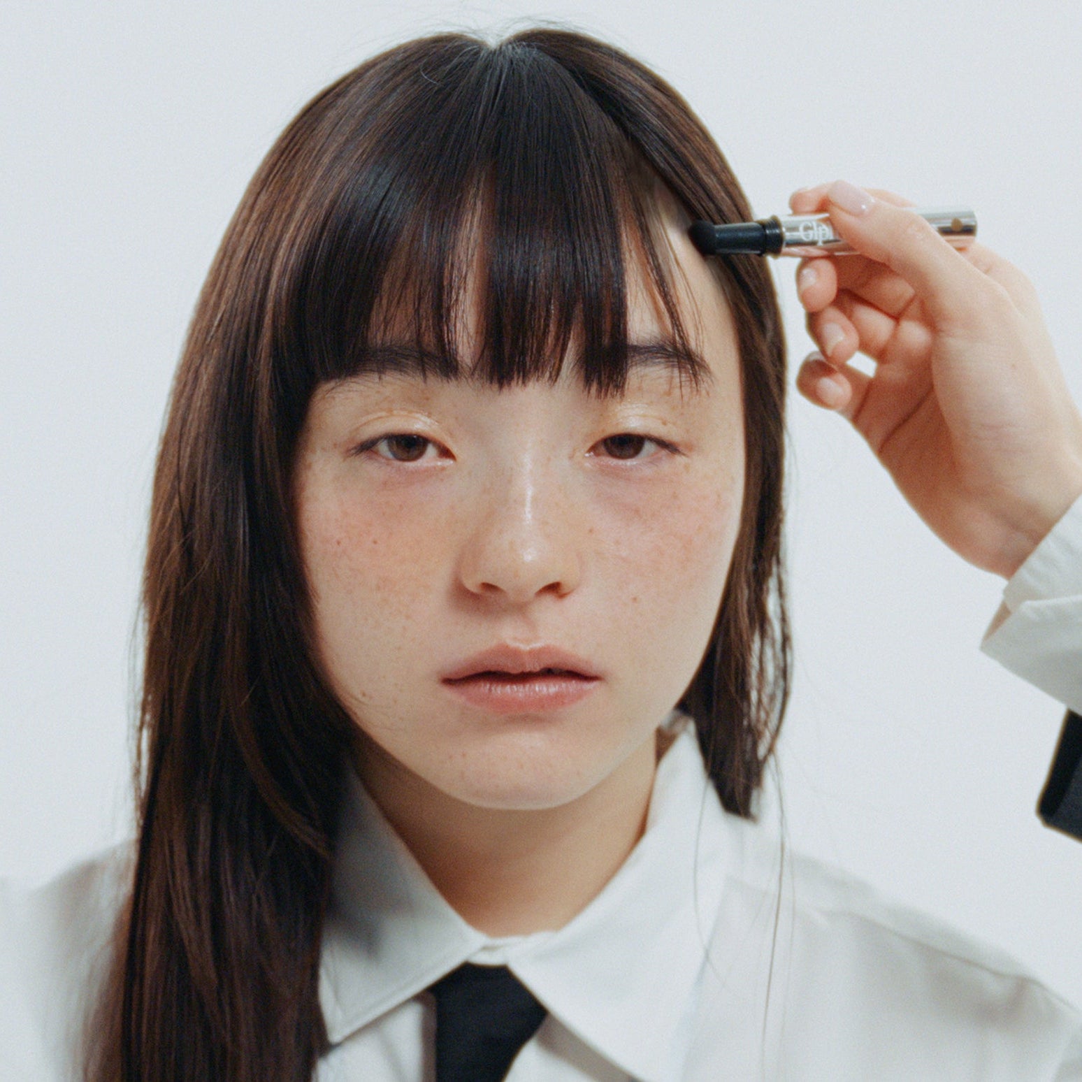 GLPHYO Hairline Maker 1.5g, appliqué sur la ligne de cheveux; main tenant le produit, jeune femme devant un fond clair.