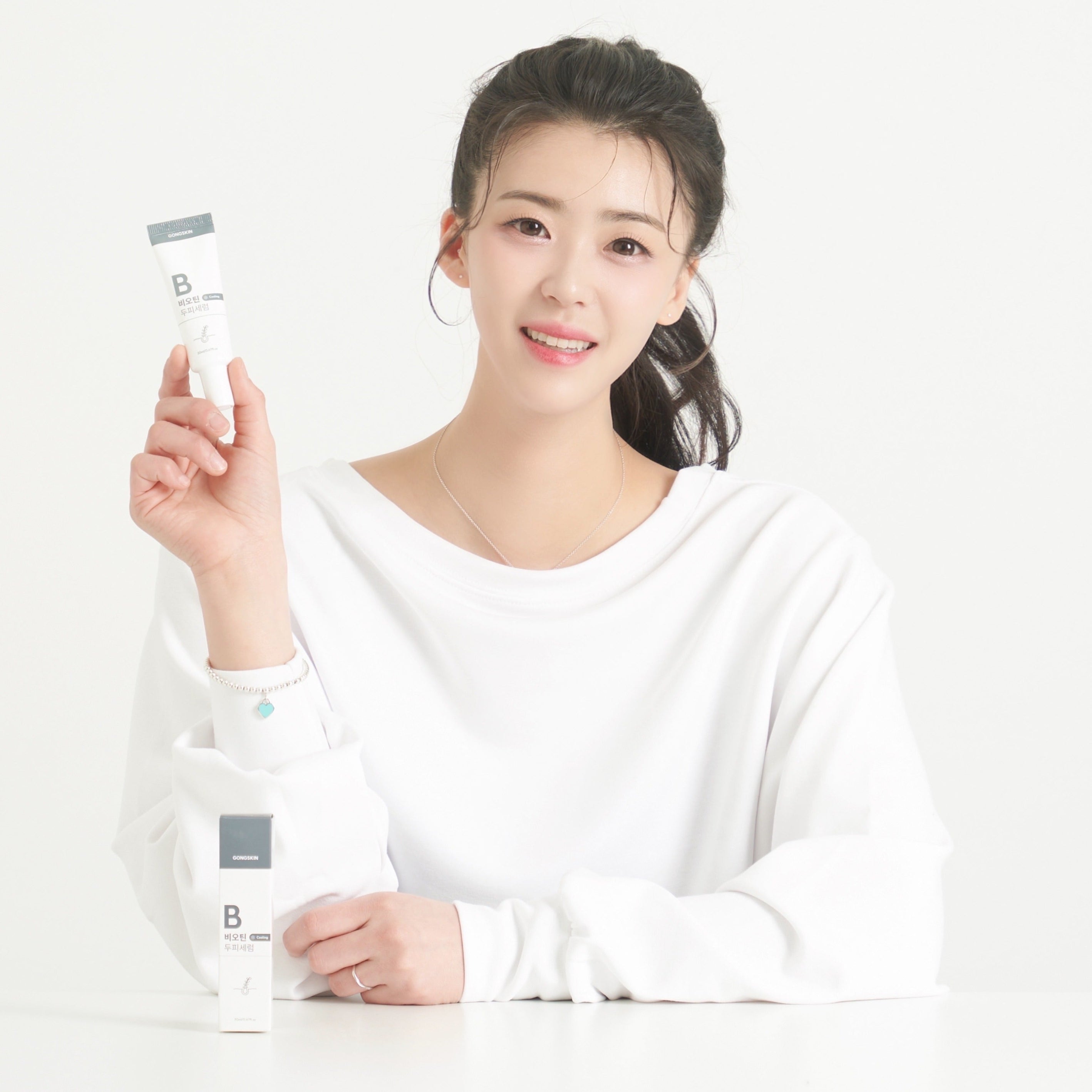 Décris l'image en français : GONGSKIN  Biotin Cooling Scalp Serum 20ml, marque montrée par une femme tenant le flacon sur fond clair.