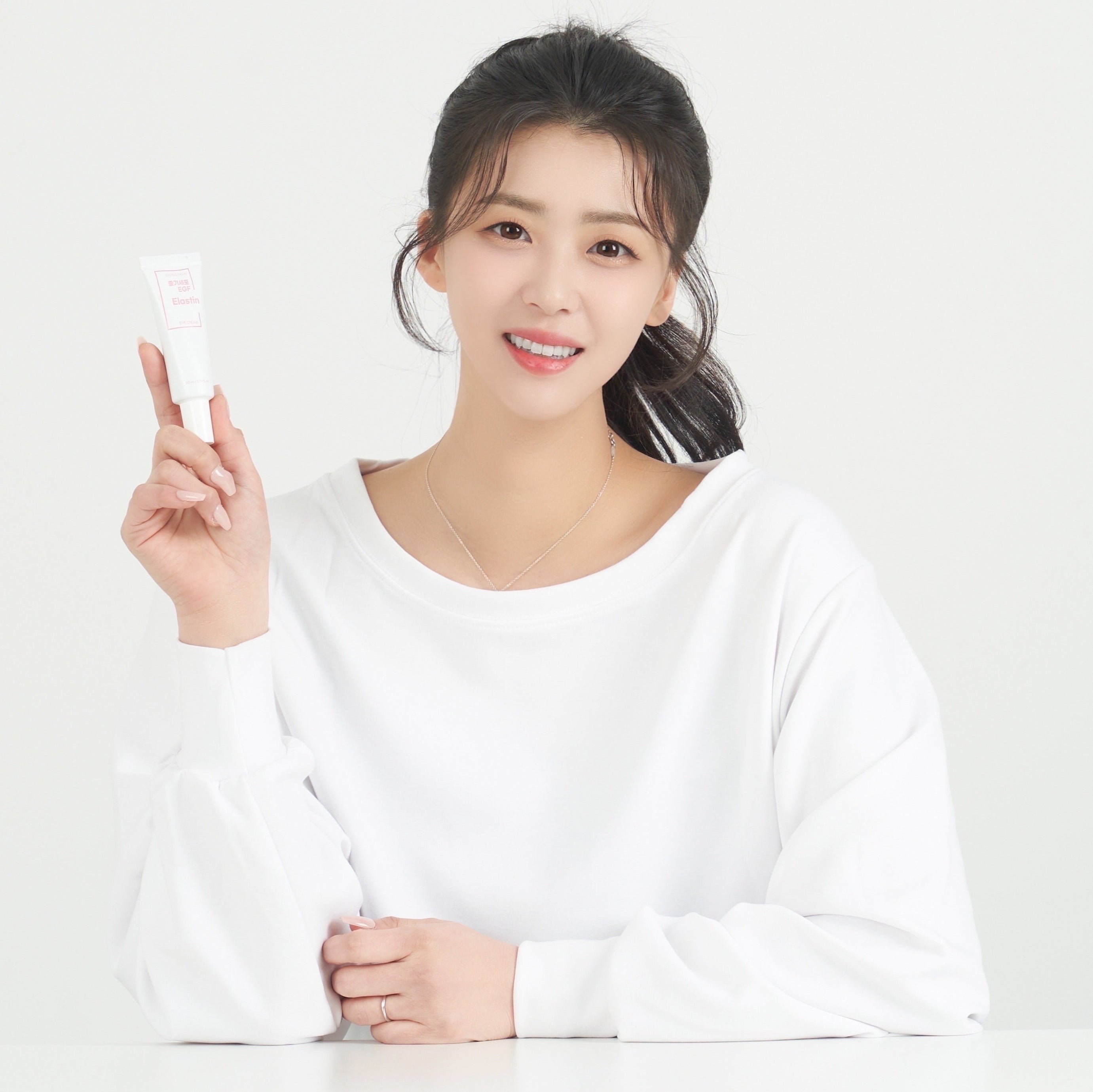 Décris l'image en français : GONGSKIN  Stem Cell EGF Elastin Eye Cream 20ml, tube tenu par une femme souriante, fond clair.