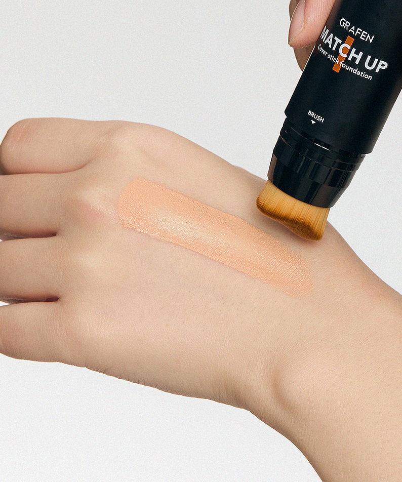 GRAFEN  Match Up Cover Stick Foundation 12g : main appliquant un fond de teint stick avec swatch sur peau, fond clair.