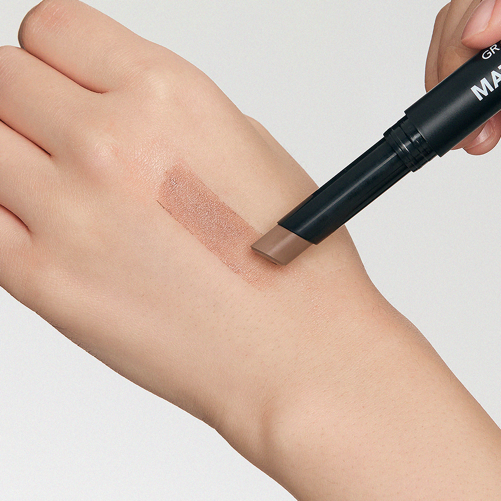 GRAFEN  Match Up Shading Stick Neutral Brown 1.8g, main appliquant un trait de maquillage sur peau, fond clair.
