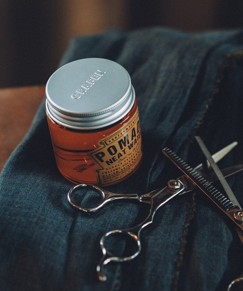 GRAFEN  Pomande Neat Water 100g : pot orange sur tissu bleu avec ciseaux et rasoir, ambiance barber shop