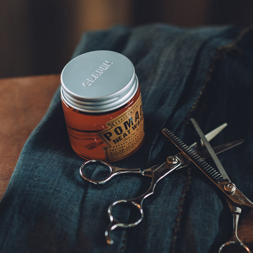 GRAFEN  Pomande Neat Water 100g : pot orange sur tissu bleu avec ciseaux et rasoir, ambiance barber shop