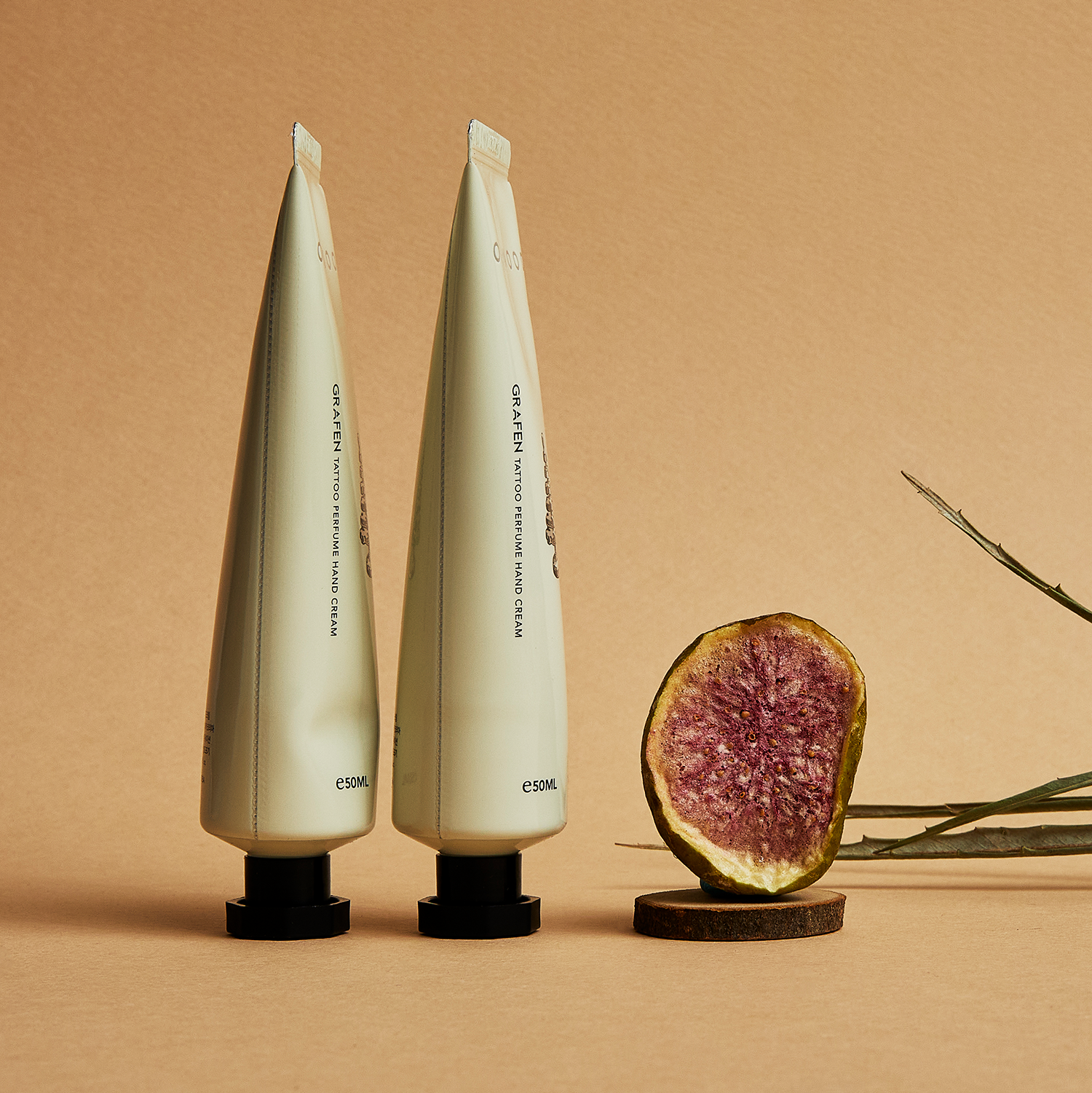 GRAFEN  Tattoo Perfume™ One Wood Hand Cream 50ml : crème mains sur fond beige, tubes près d’un fruit et brindille.