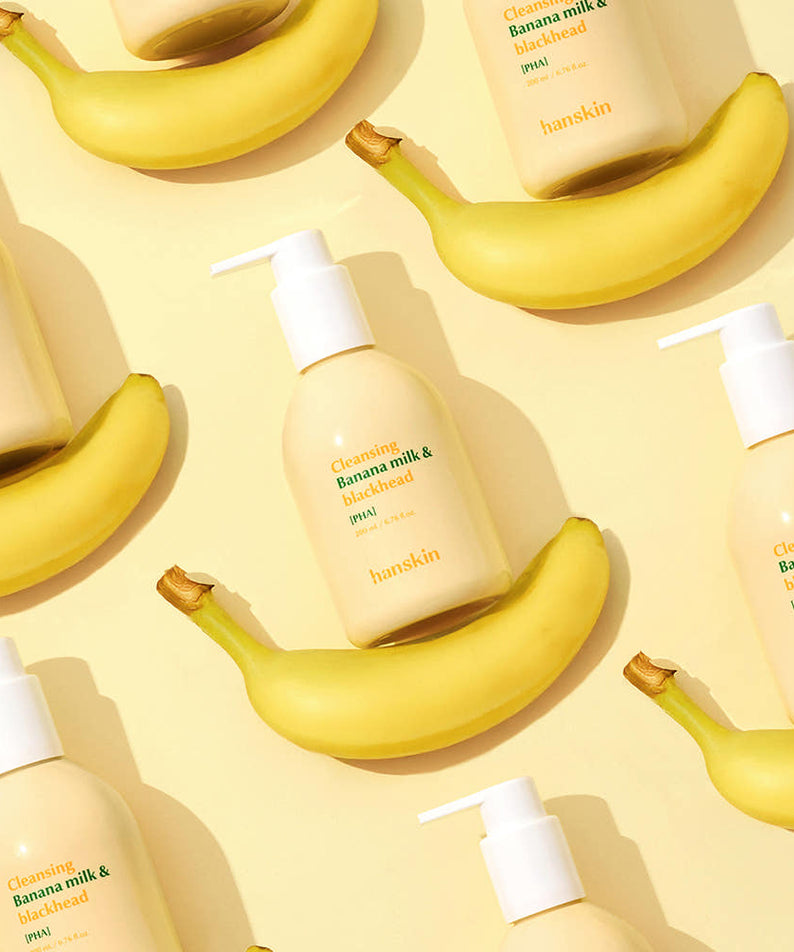 Décris l'image en français : HANSKIN Cleansing Banana Milk & Blackhead PHA 200ml, flacons et bananes sur fond jaune ensoleillé.
