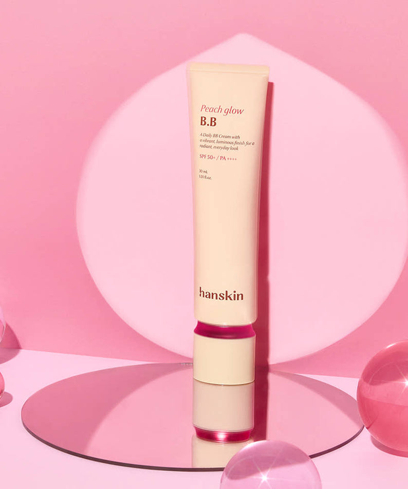 HANSKIN Peach Glow BB Cream 30ml, tube sur fond rose, ambiance maquillage, marque HANSKIN en contexte visuel beauté.
