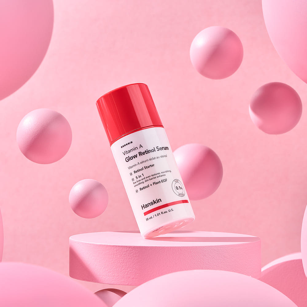 HANSKIN Vitamin A Glow Retinol Serum 30ml sur socle rose, marque HANSKIN, bouteilles et sphères décoratives, fond pastel.