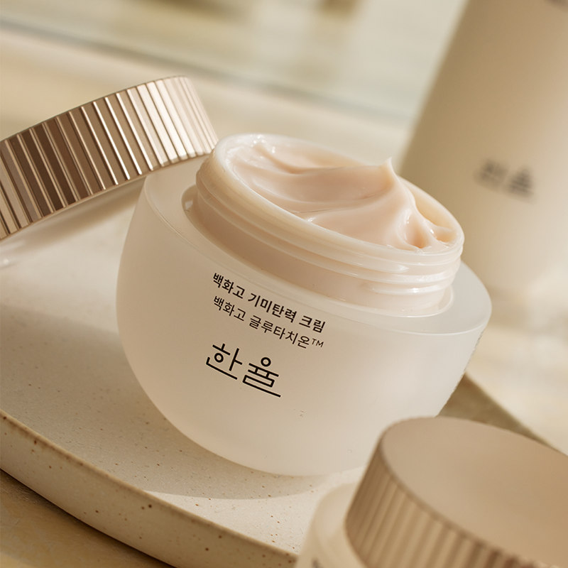 Décris l'image en français : HANYUL Baekhwago Gimitanryuk Eye Cream 25ml, crème sous pot, sur fond beige.