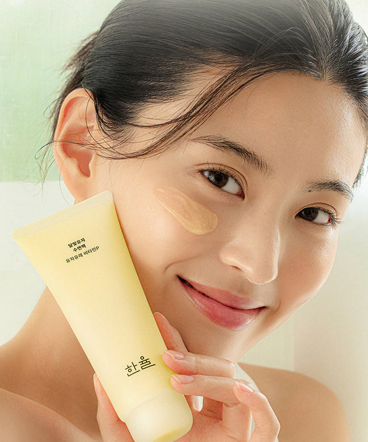 HANYUL Moonlight Yuja Sleeping Pack 100ml de HANYUL, sur visage féminin tenant le tube, ambiance spa lumineuse