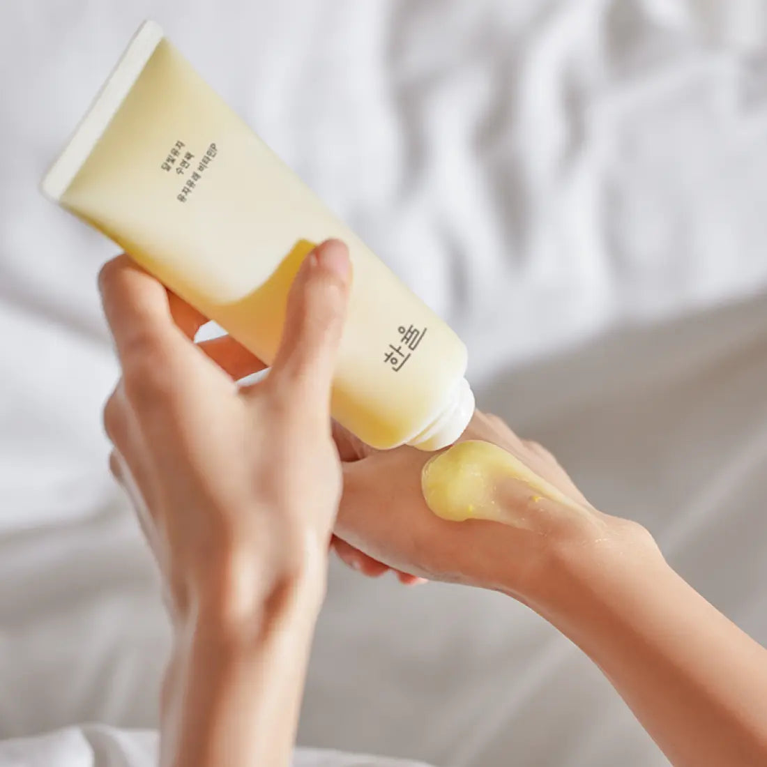 HANYUL Moonlight Yuja Sleeping Pack 100ml, tube jaune, mains appliquant un soin sur peau, décor chambre spa