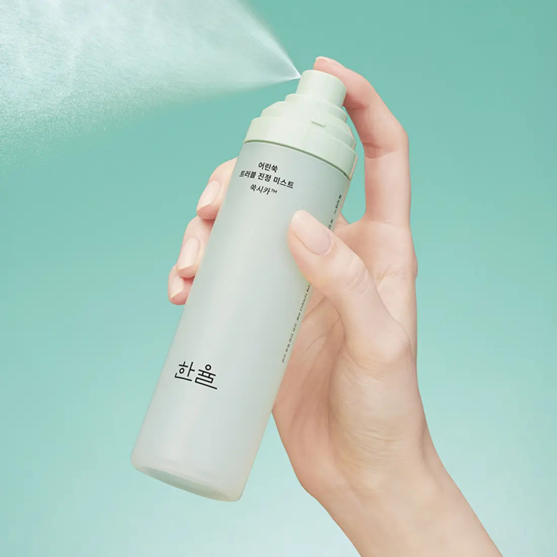 HANYUL Young Artemisia Trouble Mist 120ml, flacon brume anti-imperfections HANYUL, main tenant le produit sur fond turquoise