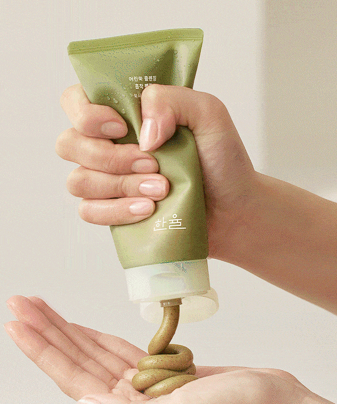 Une main utilisant le HANYUL Young Mugwort Cleansing absorption Pack Foam, produit de soins pour la peau à base d'armoise verte.