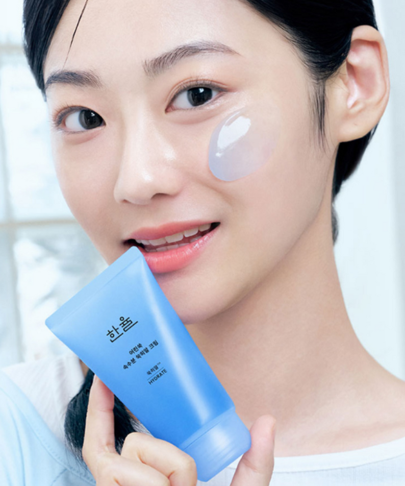 Femme souriante tenant un tube de HANYUL Young Artemisia Extract Moisturizing Cream 60ml sur fond lumineux.