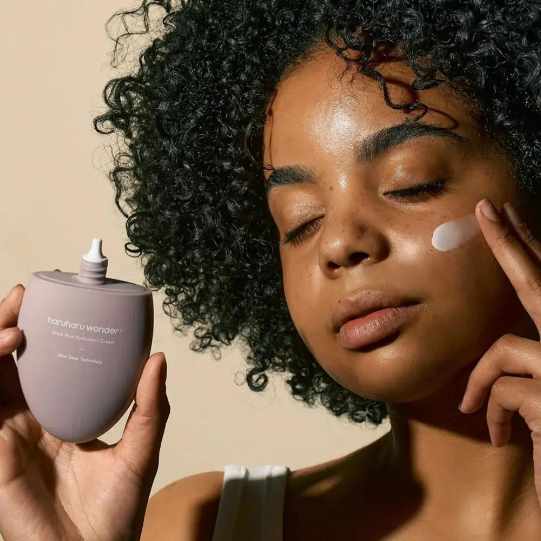 HARUHARU Black Rice 10 Hyaluronic Cream 50ml, femme aux cheveux bouclés appliquant la crème hydratante, tube et pot.