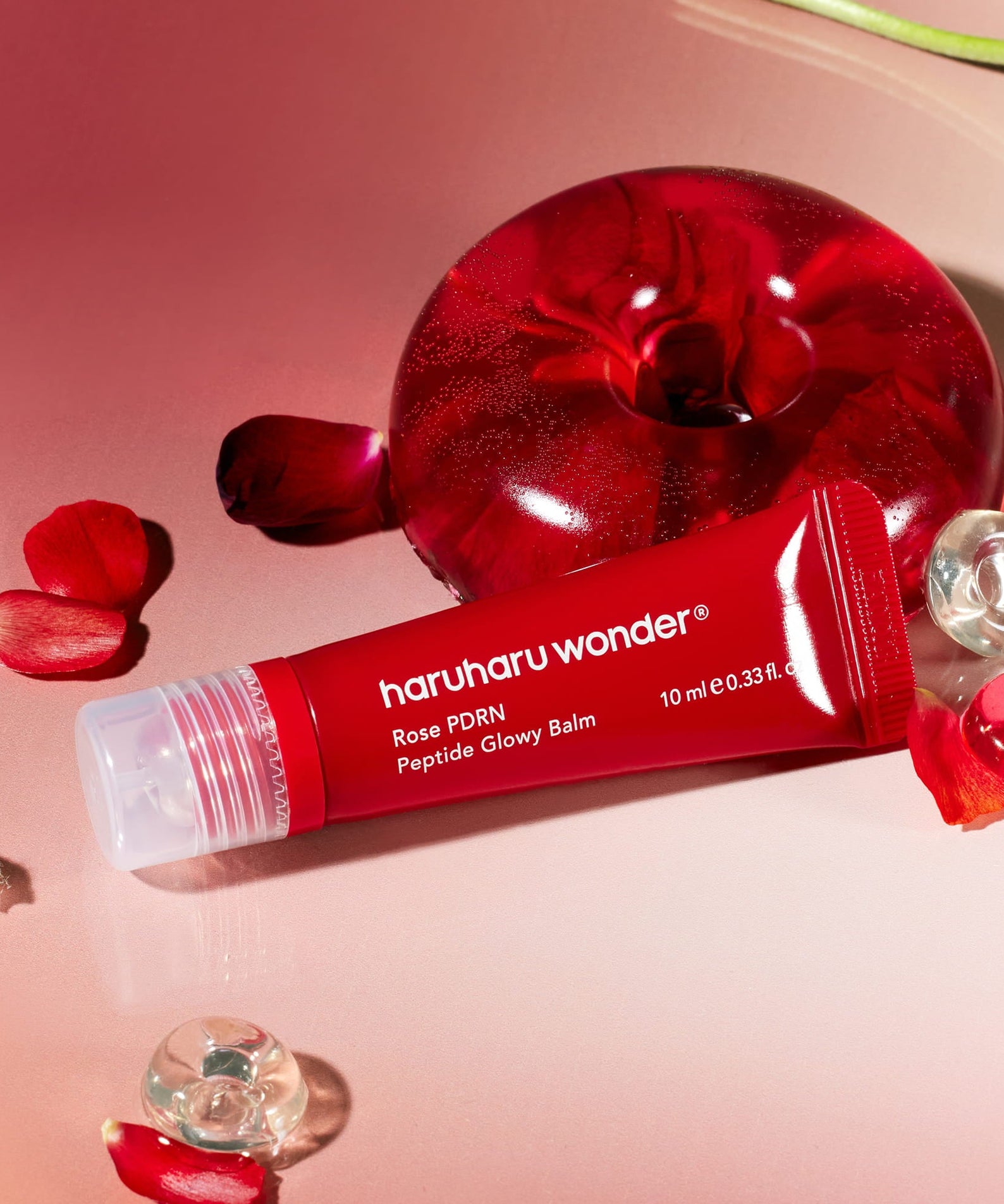 HARUHARU Rose PDRN  Peptide Glowy Balm 10ml, tube rouge sur fond rose, marque HARUHARU, fleurs et gouttes de sérum