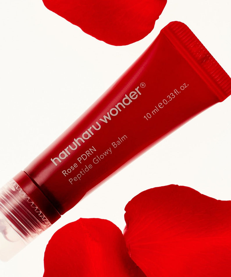 Décris l'image en français : HARUHARU Rose PDRN  Peptide Glowy Balm 10ml, tube rouge et pétales roses sur fond clair.