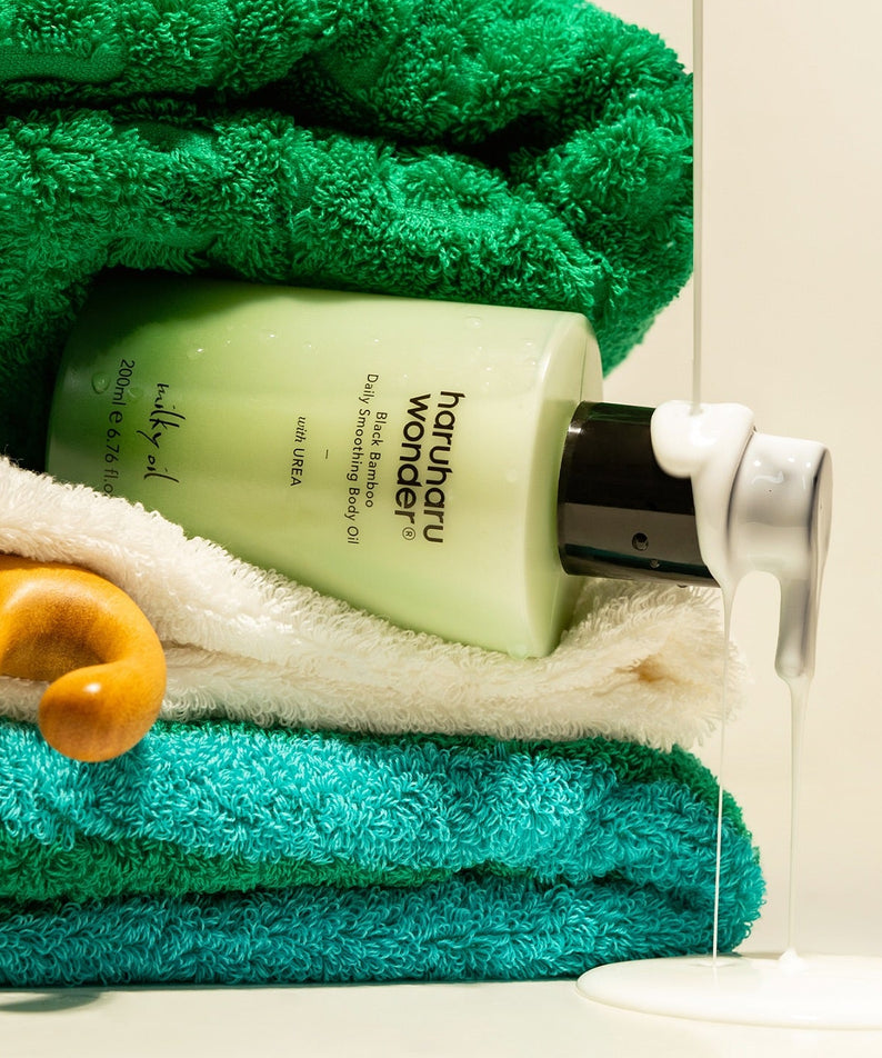 HARUHARU Black Bamboo Daily Smoothing Body Oil 200ml avec serviettes vertes et blanches, idéal pour une peau lisse et hydratée.