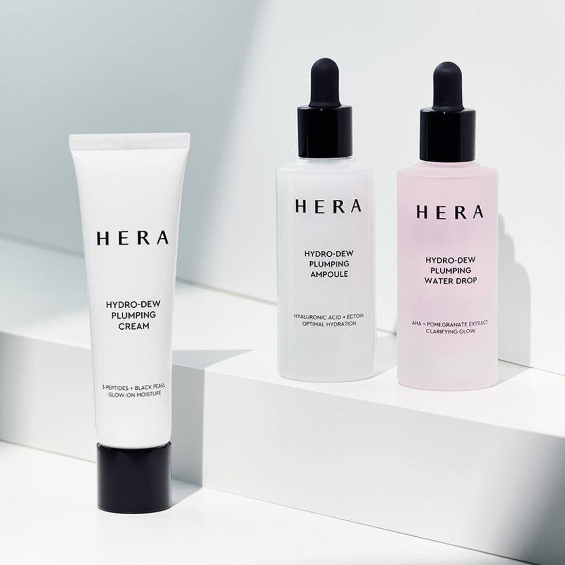 Décris l'image en français: HERA Hydro-Dew Pluming Water Drop 50ml de la marque HERA, flacon sur fond blanc minimaliste.