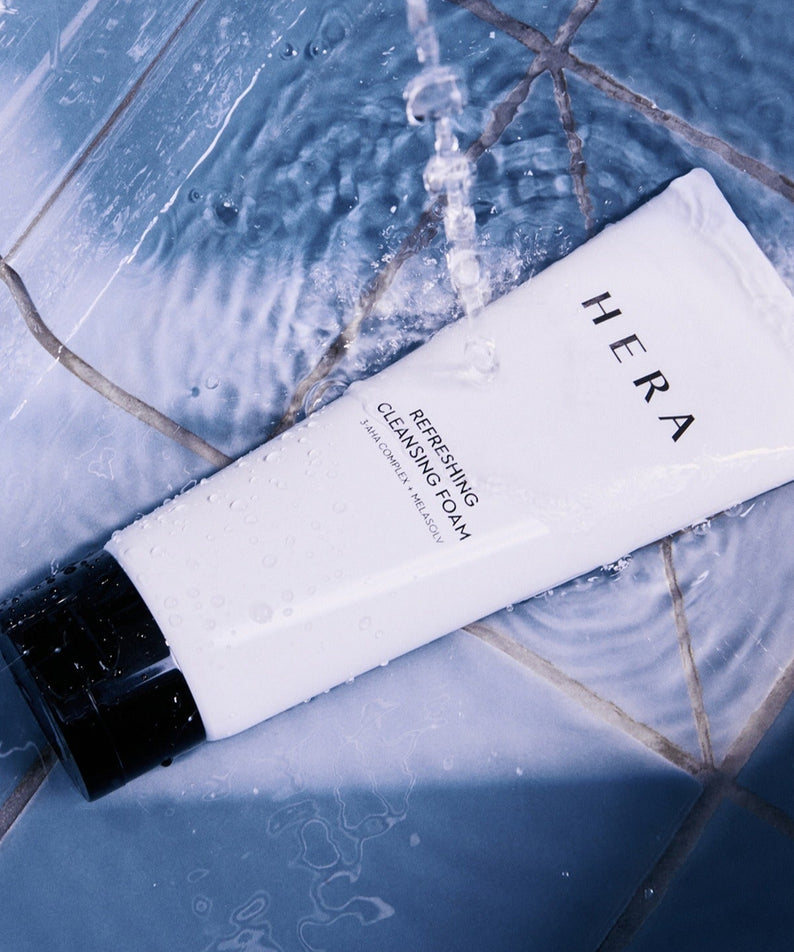 HERA Refreshing Cleansing Foam 160g de HERA sur carrelage bleu avec mousse et éclaboussures, contexte soins visage