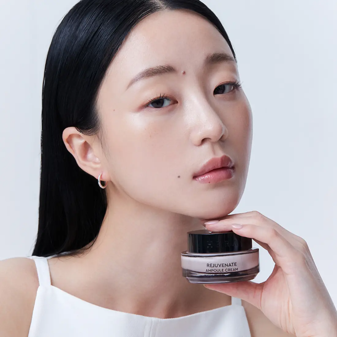 HERA Rejuvanate Ampoule Cream 50ml, pot noir sur fond clair, femme maquillée posant avec la crème HERA