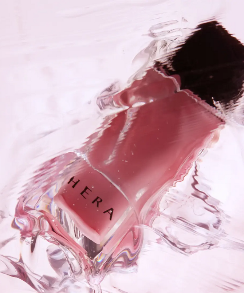 HERA  Sensual Nude Gloss 5g de HERA, sur fond clair avec texture brillante, vue produit en gros plan.