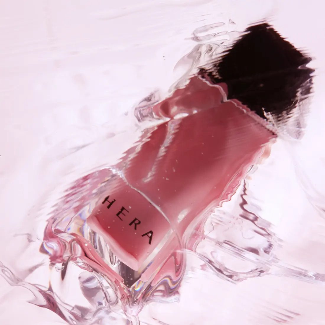 HERA  Sensual Nude Gloss 5g de HERA, sur fond clair avec texture brillante, vue produit en gros plan.